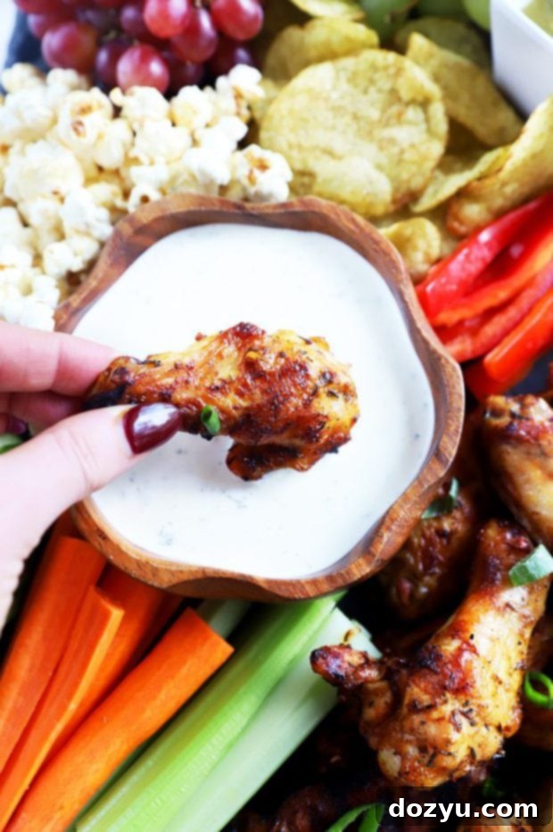 Close-up image of a chicken wing being dipped into creamy sauce, highlighting the texture and appeal