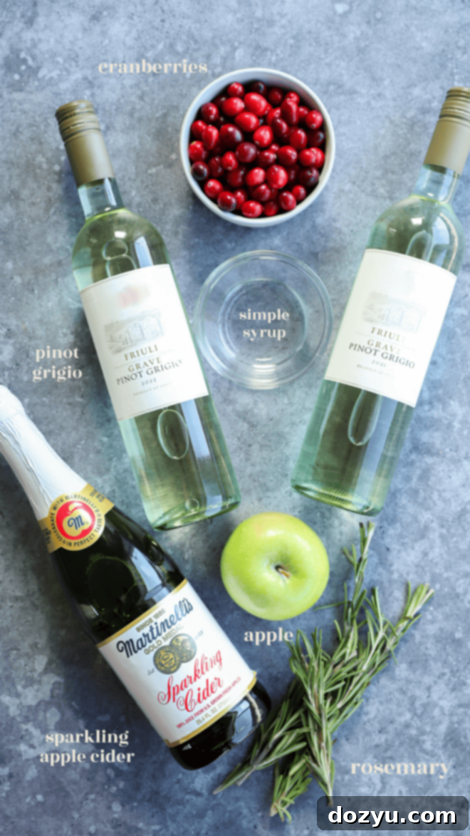 A flat lay photograph showcasing all the fresh ingredients for Christmas Sangria: white wine, sparkling apple cider, simple syrup, cranberries, granny smith apple, and rosemary.