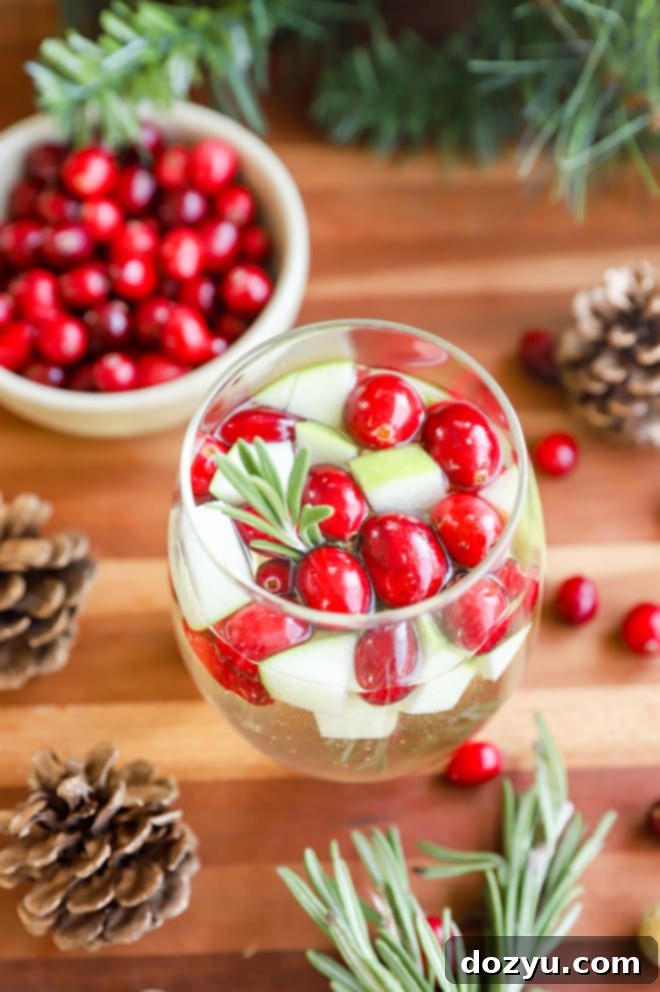 A single glass of white Christmas Sangria ready to be enjoyed, with a sprig of rosemary and cranberries.