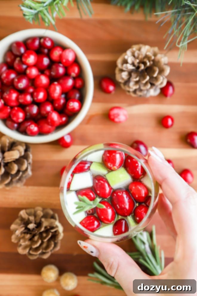 A hand holding a stemless wine glass filled with refreshing Christmas Sangria, showing the festive colors.