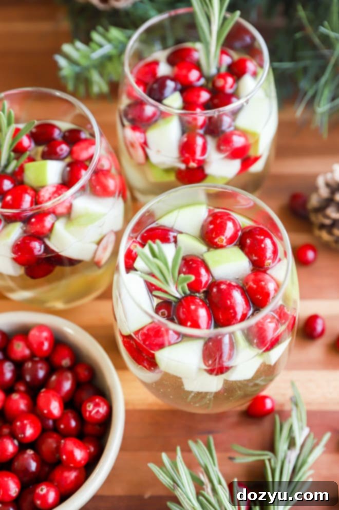 Glasses of easy white wine Christmas Sangria arranged beautifully with fresh fruit and herbs.