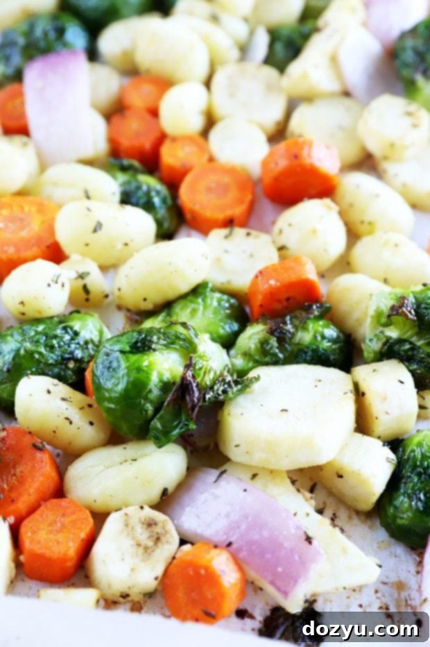 Close-up of golden-brown gnocchi and vibrant roasted carrots, parsnips, and Brussels sprouts on a sheet pan.