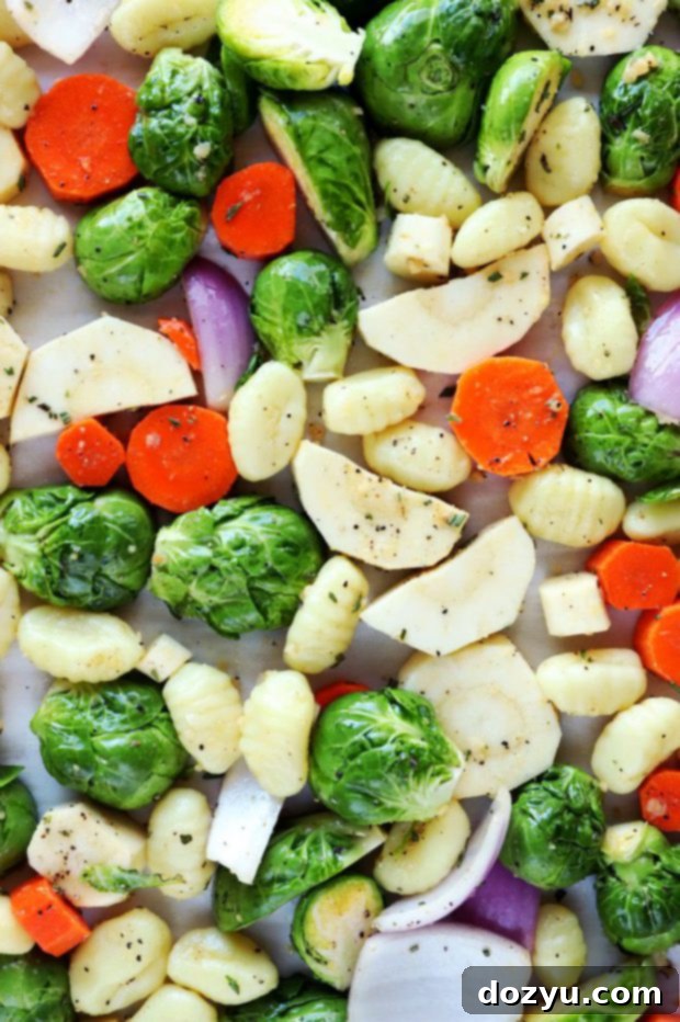 Uncooked gnocchi and chopped winter vegetables tossed with olive oil and seasoning in a large mixing bowl.