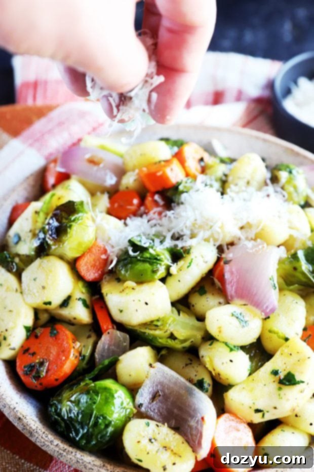 A generous portion of roasted sheet pan gnocchi and tender vegetables plated, garnished with fresh basil and cheese.