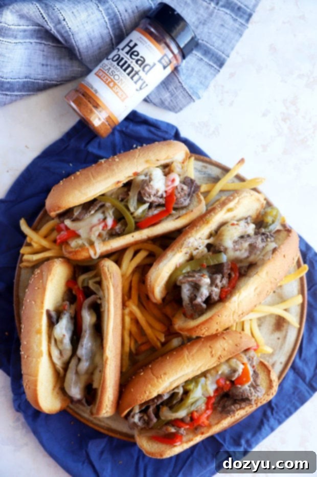 An overhead view of two assembled Philly cheesesteaks, generously filled with seasoned beef, peppers, and melted cheese on toasted buns.