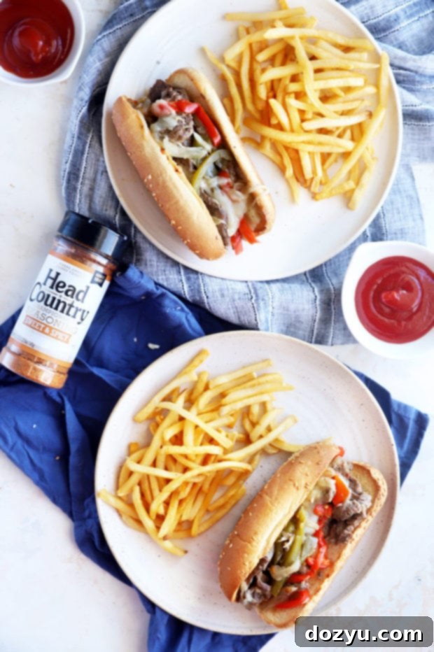 A mouth-watering close-up of two Instant Pot Philly Cheesesteaks on toasted hoagie rolls, with melted cheese dripping over the seasoned beef and vegetables, served with a side of fries.