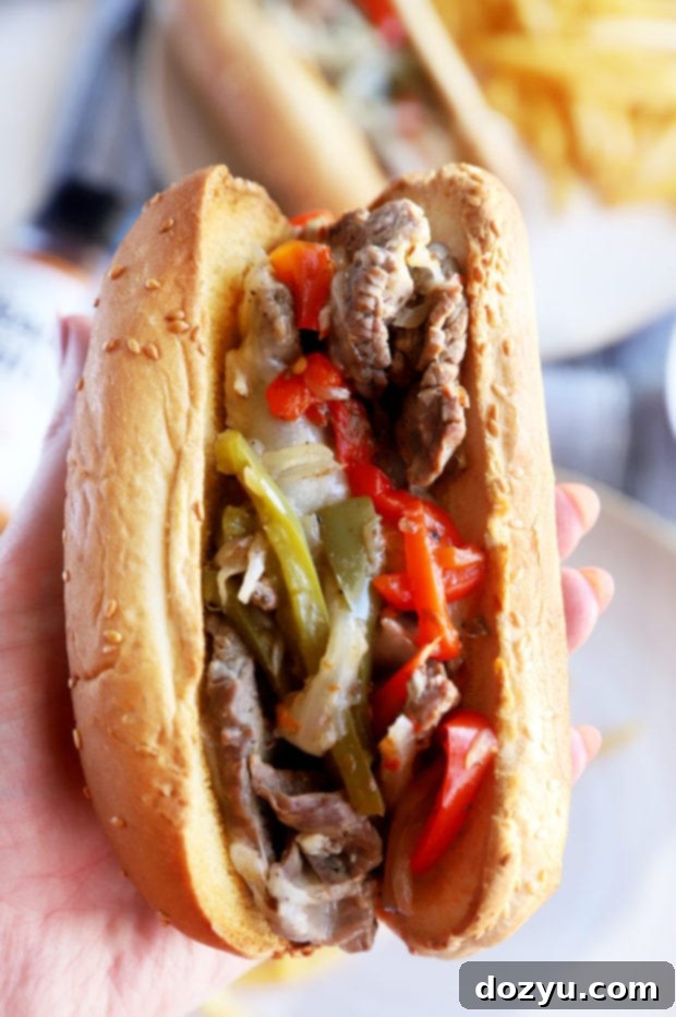 A hand holds a perfectly assembled Instant Pot Philly Cheesesteak, revealing the rich filling and melted cheese, against a blurred background.