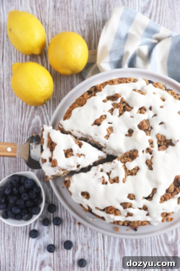 A close-up image of a full Blueberry Lemon Streusel Coffee Cake on a rustic wooden board, showing the golden streusel topping and generous drizzle of lemon cream cheese glaze.