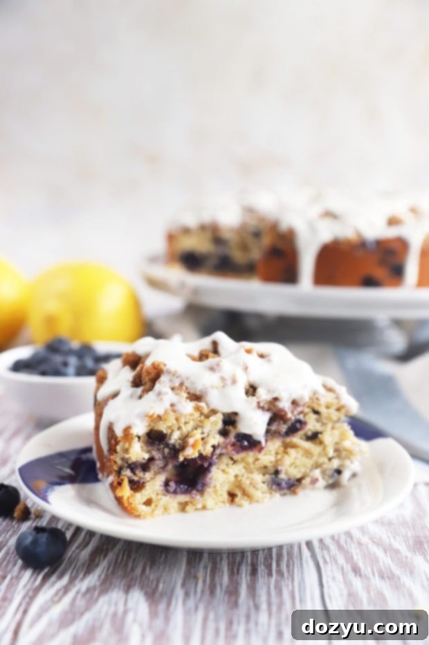 A close-up of a slice of Blueberry Lemon Streusel Coffee Cake on a plate, featuring plump blueberries, a crumbly streusel topping, and a delicate lemon glaze.