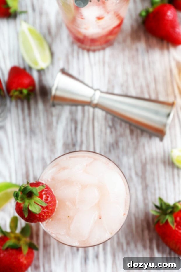 Overhead image of a vibrant Strawberry Tequila Fizz cocktail, garnished with fresh strawberries and lime slices, on a light surface.