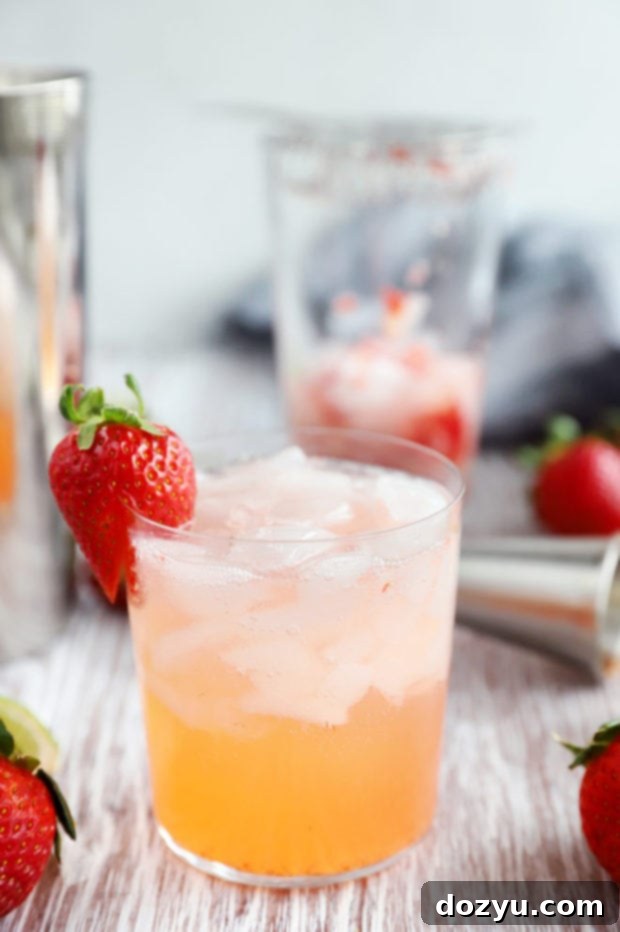 Close-up of a Strawberry Tequila Fizz cocktail in a double old fashioned glass, with sliced strawberries visible inside.