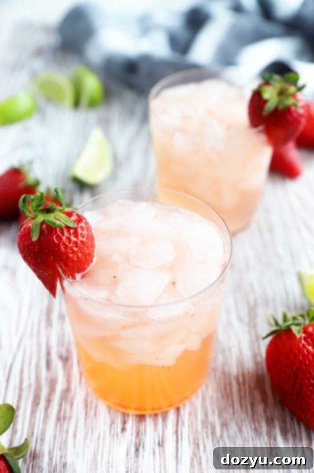 Photograph of a Strawberry Tequila Fizz cocktail in a stylish glass, garnished with fresh strawberries, on a rustic wooden surface.