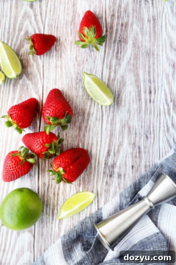 Overhead photo showing fresh strawberries and limes, key ingredients for a Strawberry Tequila Fizz, arranged on a light surface.