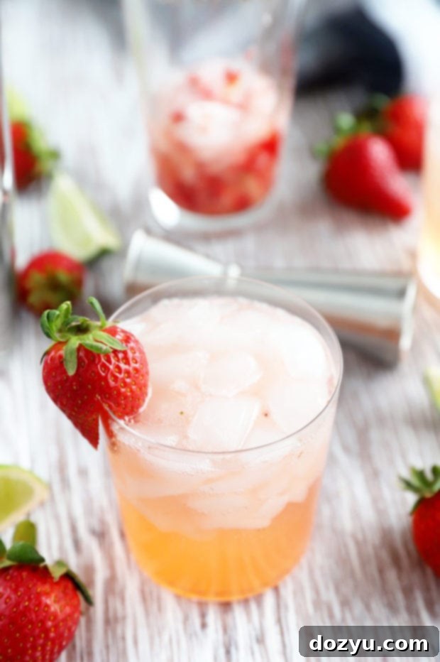 Close-up of a single Strawberry Tequila Fizz cocktail in a glass, with a garnish of a whole fresh strawberry on the rim.