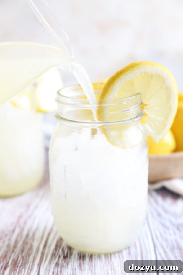 Hand pouring homemade lemonade into a glass pitcher