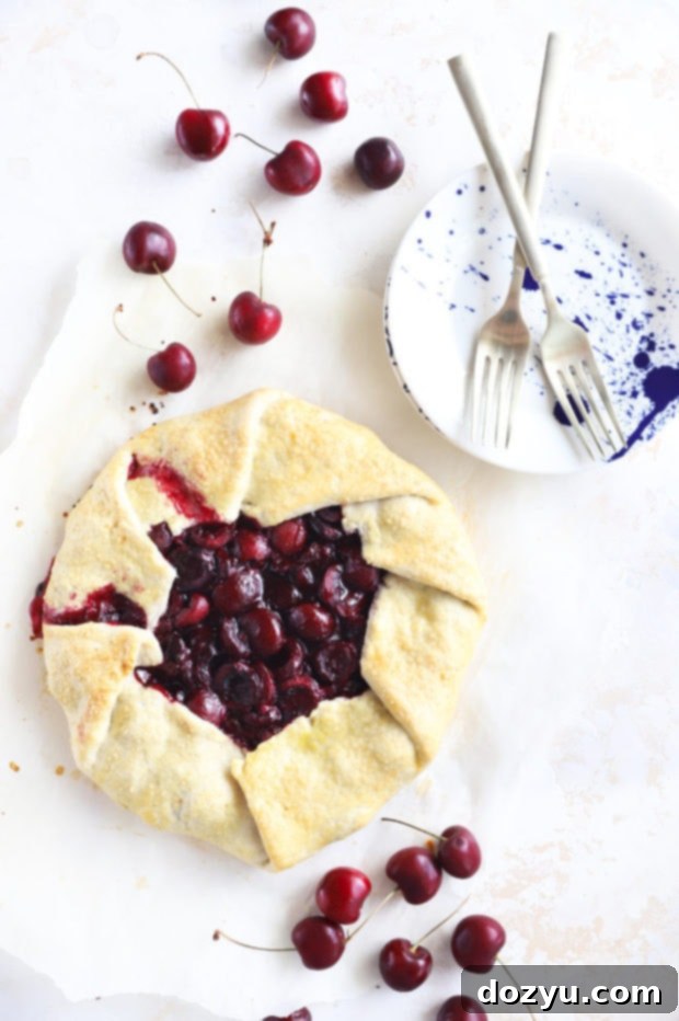 Overhead shot of a rustic Brandy Cherry Galette cooling on a wire rack, surrounded by fresh cherries