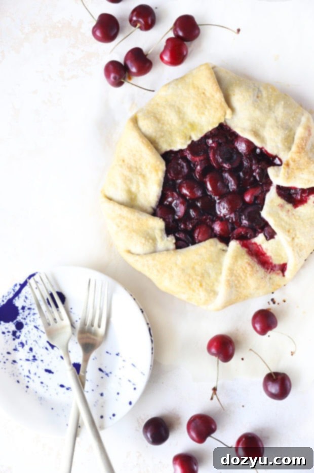 Overhead image of a Brandy Cherry Galette, with fresh cherries scattered around it on a wooden surface
