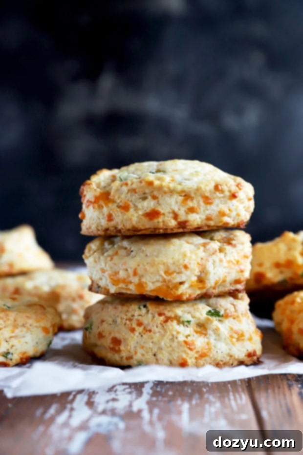A side view of a towering stack of freshly baked cheddar biscuits, emphasizing their height and golden crust.