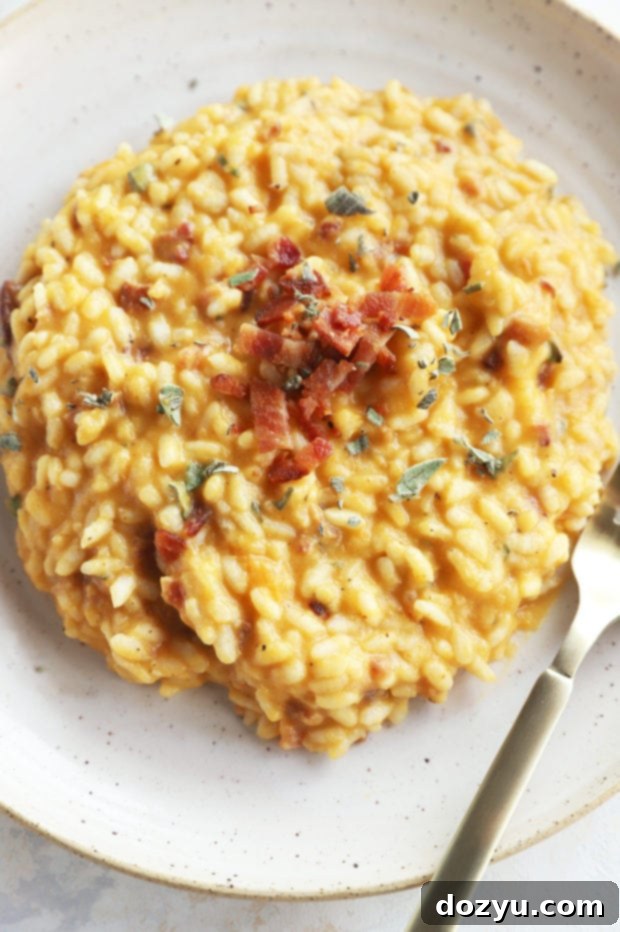A serving of Bacon Butternut Squash Risotto on a white plate, garnished with fresh sage leaves.