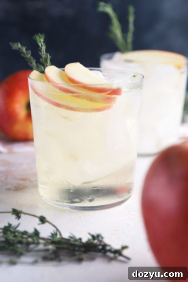 Side view of a Thyme Apple Gin and Tonic in a tall glass, garnished with apple slices and a thyme sprig
