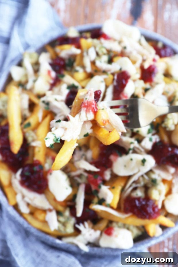Close-up image of a fork lifting a spoonful of Thanksgiving poutine, showing the melted cheese curds, gravy-soaked fries, and pieces of turkey and stuffing