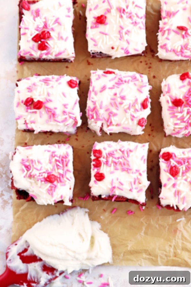 An overhead shot of red velvet brownies freshly frosted with Champagne Cream Cheese Frosting, with a spatula showing the creamy texture of the frosting.