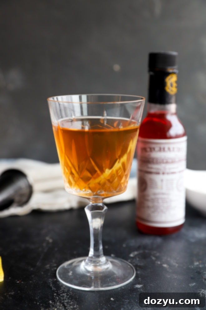 Hand pouring Peychaud's Bitters into a glass with a sugar cube for a Sazerac cocktail