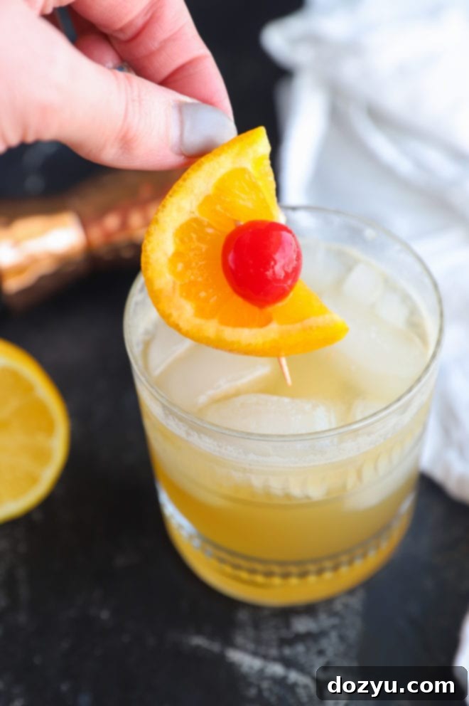 A skilled hand in the process of garnishing a freshly made whiskey sour cocktail with an orange twist.