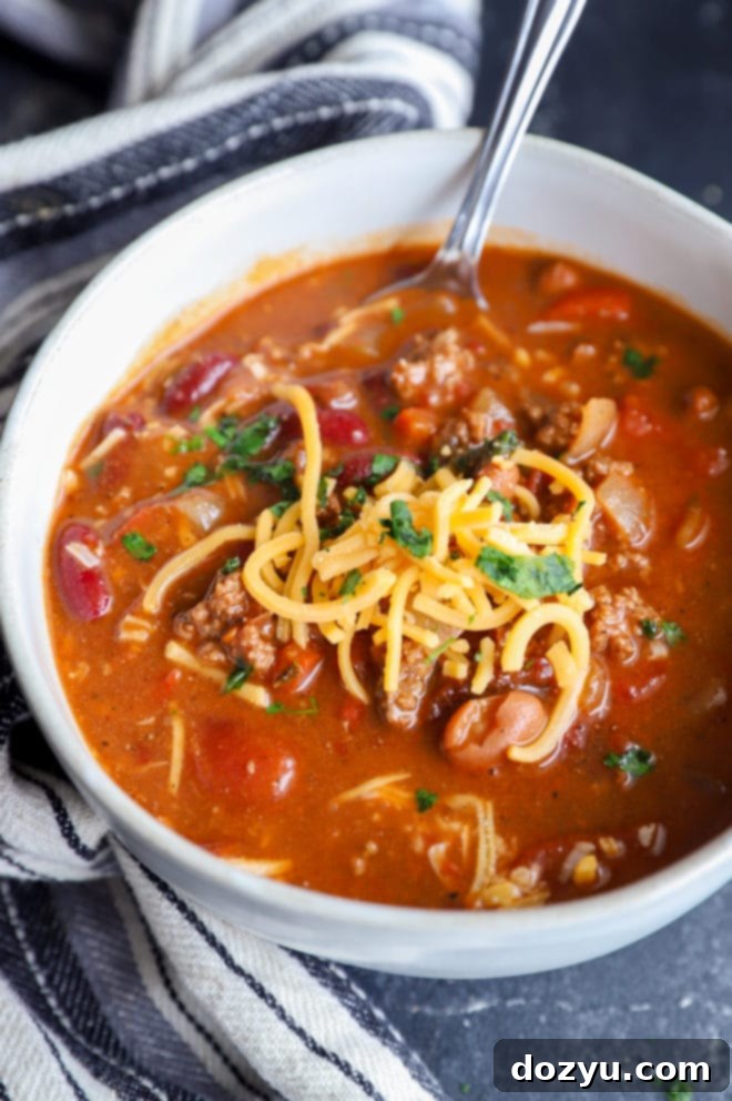 A spoon emerging from a bowl of chipotle chili, adorned with melted cheese, highlighting the rich texture of the dish.