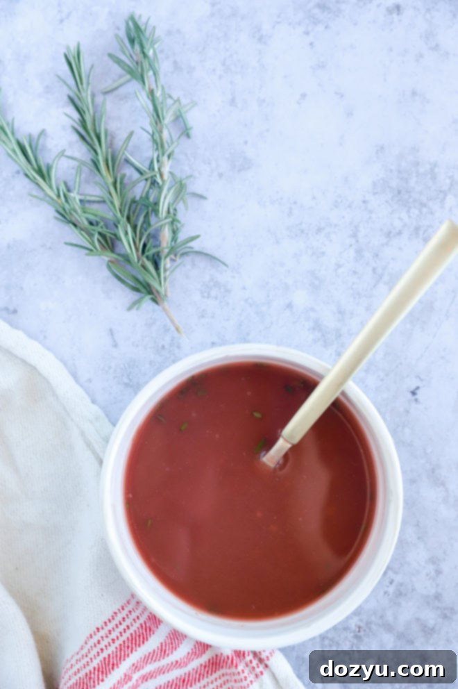 A bowl of rich red wine jus garnished with a sprig of fresh rosemary, ready to serve with savory dishes.
