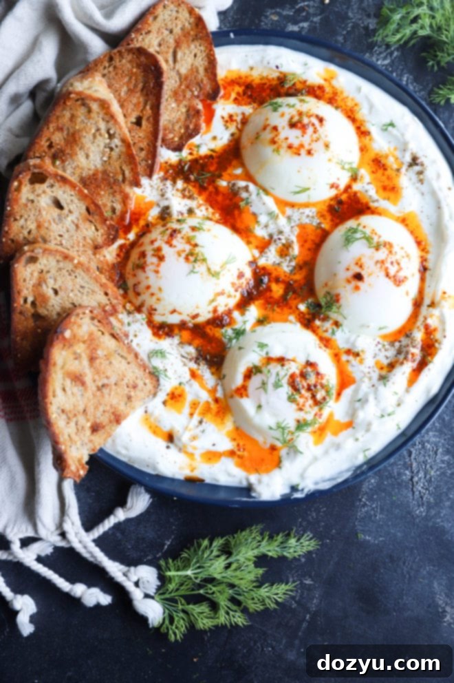 Another perspective of the Turkish Eggs, highlighting the vibrant red chili oil contrasting against the white yogurt and yellow egg yolks, with fresh dill scattered on top.