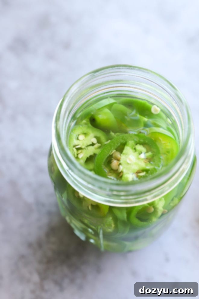 Overhead view of sliced jalapeños, serranos, and mezcal in a jar