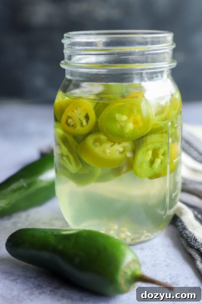 Side view of a glass jar filled with spicy infused mezcal and peppers