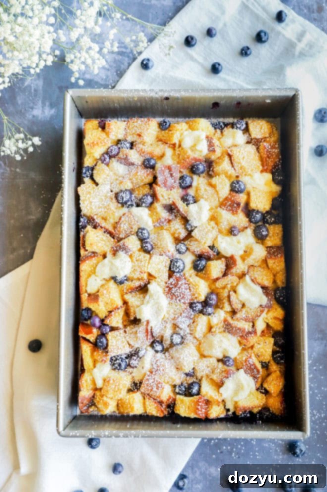 A golden-brown Blueberry Cream Cheese French Toast Casserole, fresh from the oven, with blueberries peeking through the crust.