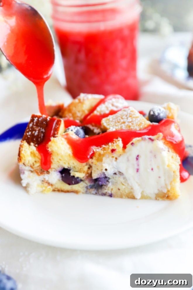 A slice of Blueberry Cream Cheese French Toast Casserole drizzled with vibrant strawberry coulis.