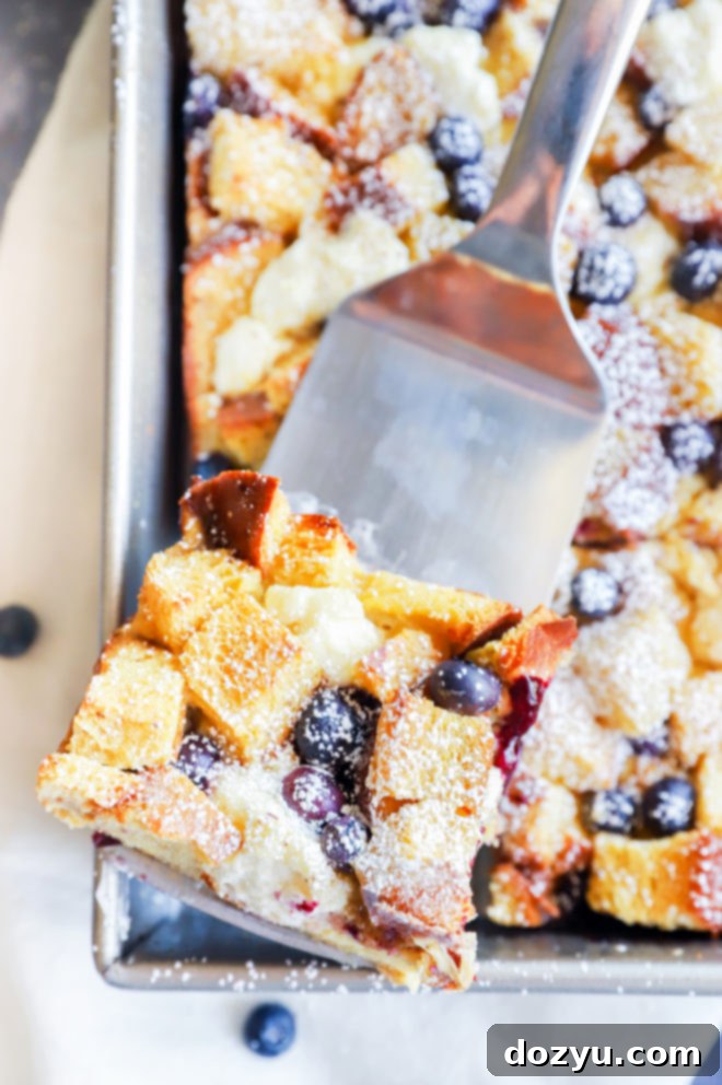 A spatula holding a delicious slice of Blueberry Cream Cheese French Toast Casserole, ready to be served.