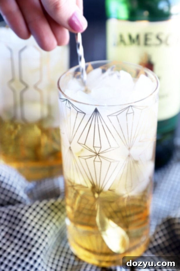 A hand stirring a Jameson and Ginger cocktail in a glass with a bar spoon.
