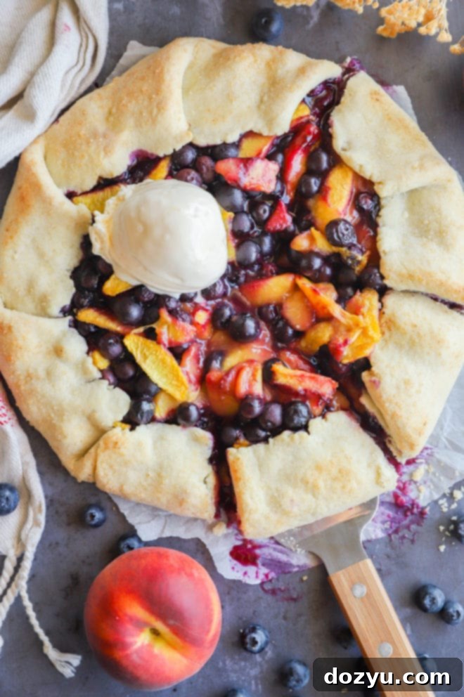 A beautiful Peach Blueberry Galette served with a scoop of vanilla ice cream, on a rustic wooden surface.