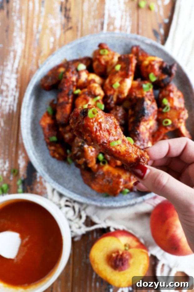 A hand holding a Bourbon Peach Grilled BBQ Wing, glistening with sauce, against a blurred outdoor background.
