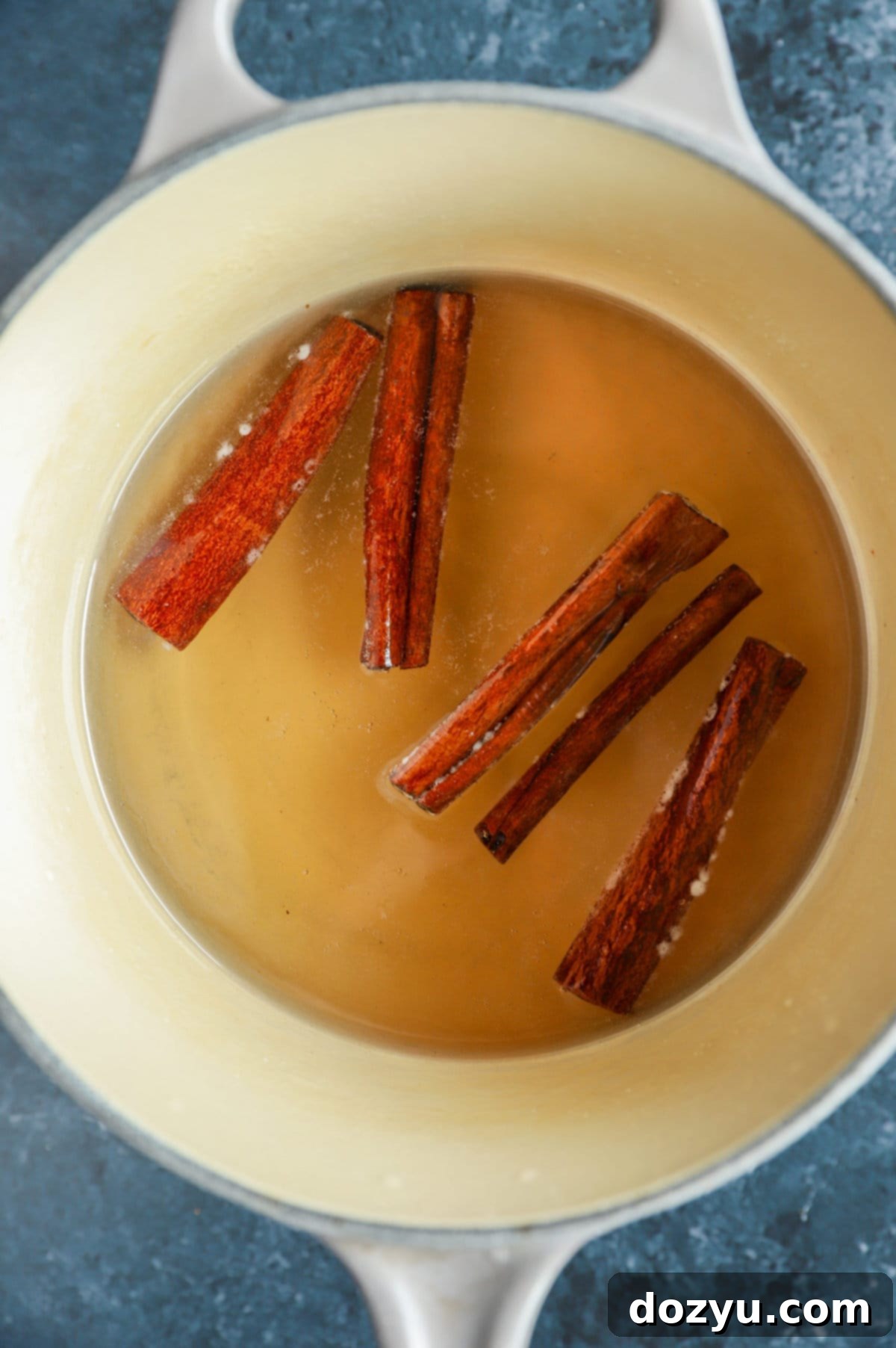 A saucepan on the stove, with cinnamon sticks and vanilla extract added to the simmering simple syrup.