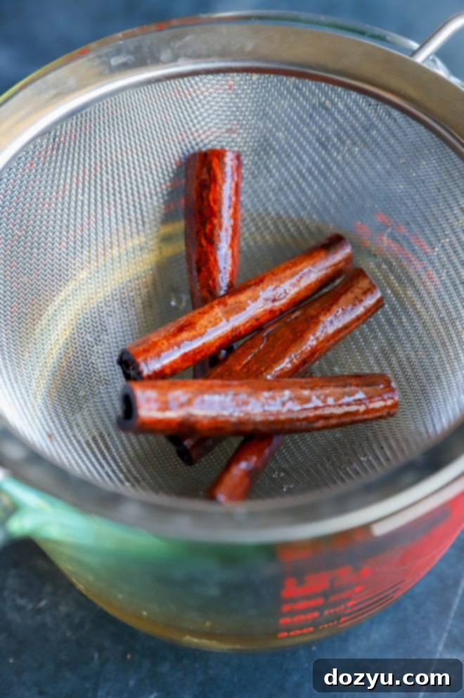 Cinnamon Simple Syrup poured into a clear glass, showing its rich amber color, with cinnamon sticks in the background.