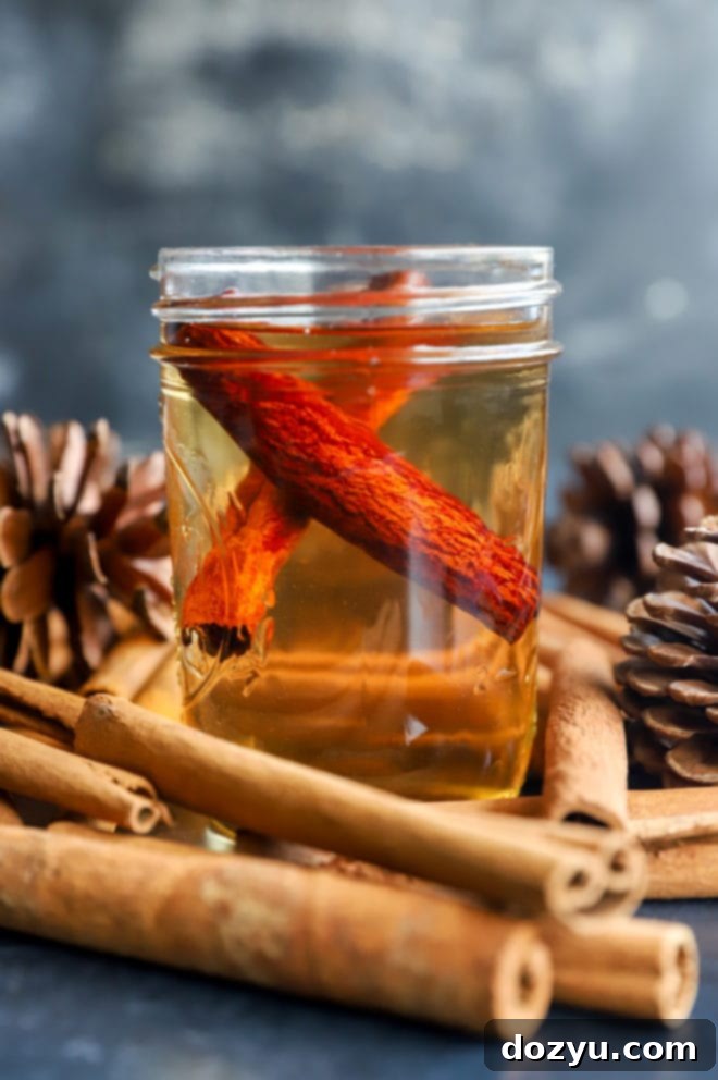 A mason jar filled with amber-colored Cinnamon Simple Syrup and cinnamon sticks, with autumn decor in the background.