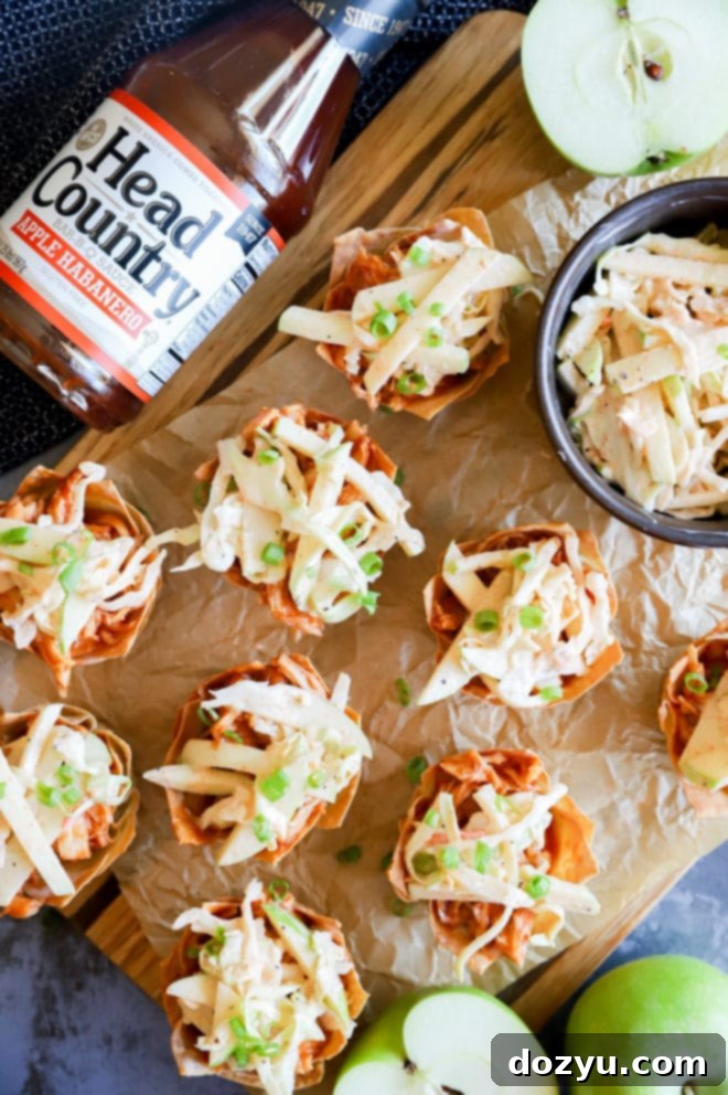 A vibrant overhead shot of Spicy BBQ Chicken Wonton Cups, showcasing the golden crispy wontons filled with shredded chicken, topped with fresh apple coleslaw and green onions. Head Country BBQ sauce bottles are visible in the background, highlighting the key ingredient.