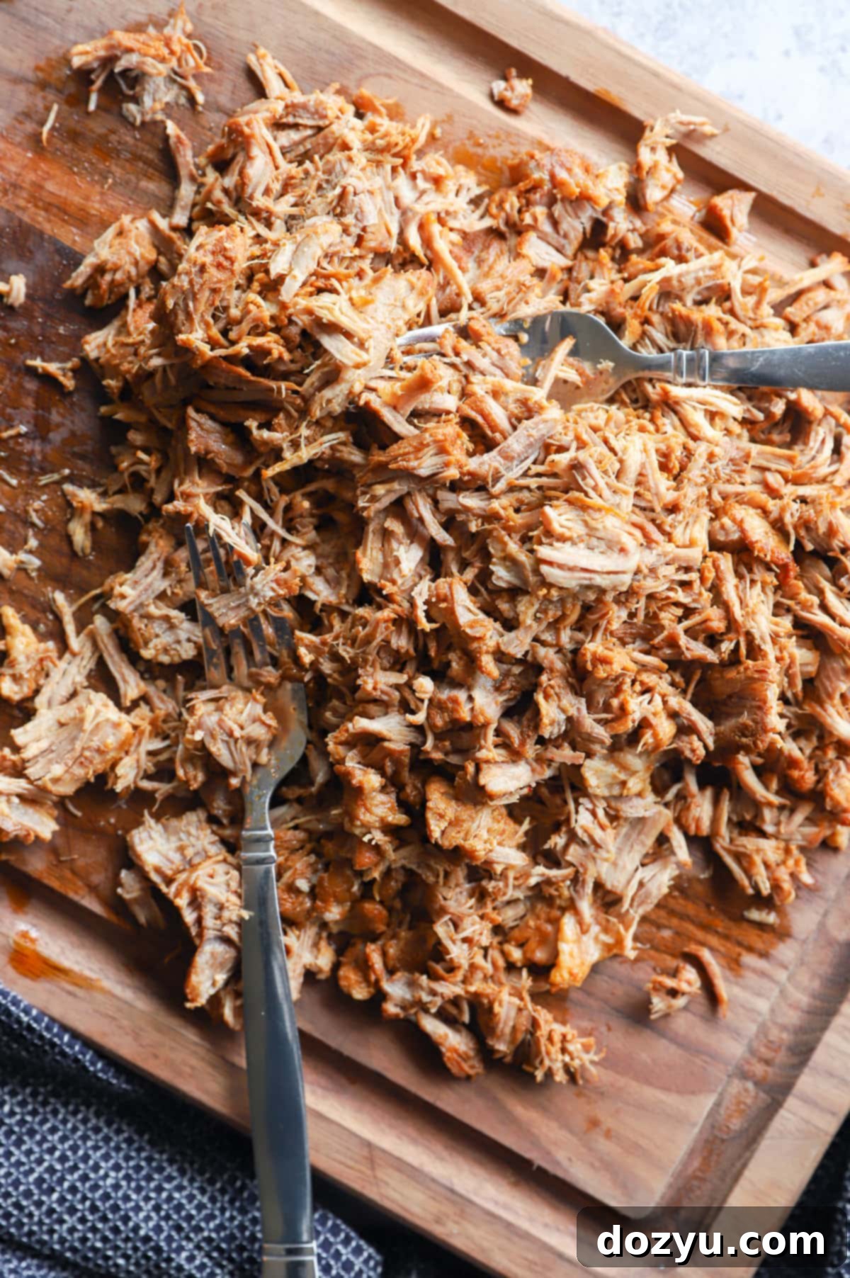 Forks shredding tender cooked pork on a cutting board