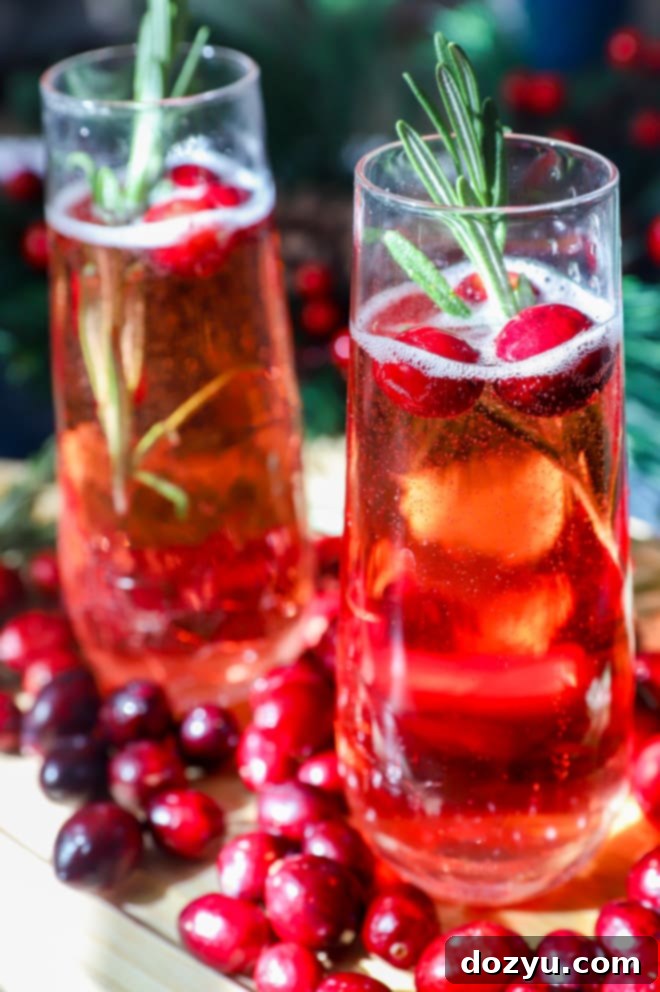 Side image of cranberry cocktails in champagne flutes, garnished with fresh cranberries and rosemary