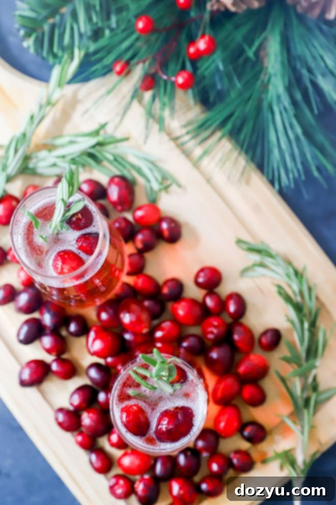 Overhead image of cranberry mimosas garnished with rosemary and cranberries, with a bottle of champagne in the background