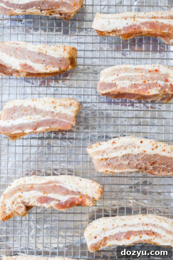 Raw AdapTable Smokey Applewood Boneless Pork Belly slices on a baking rack, ready for the oven.