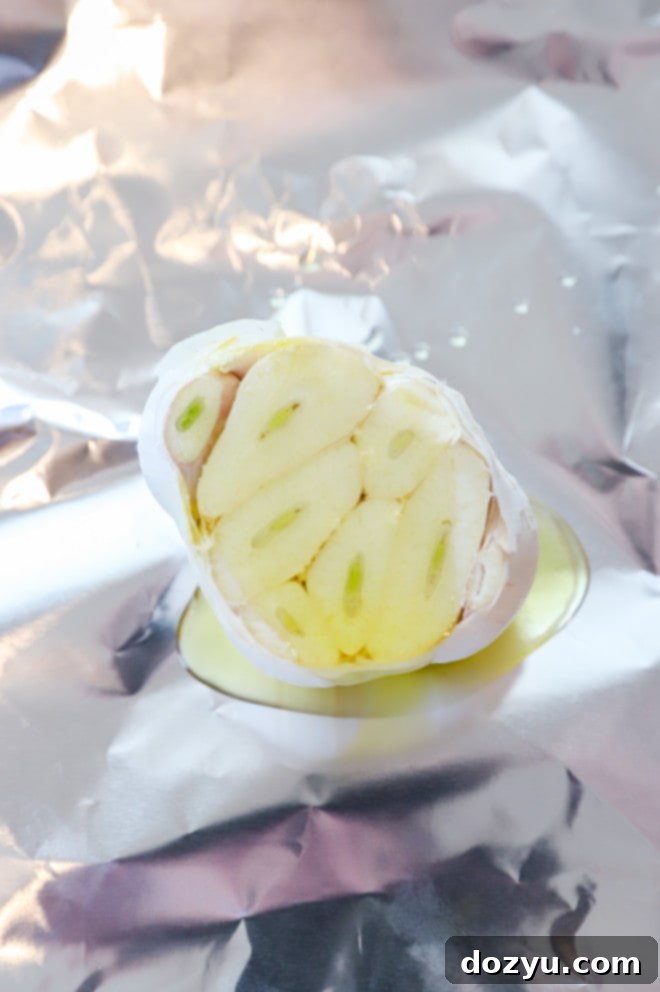 Garlic bulb generously drizzled with olive oil on a piece of aluminum foil.