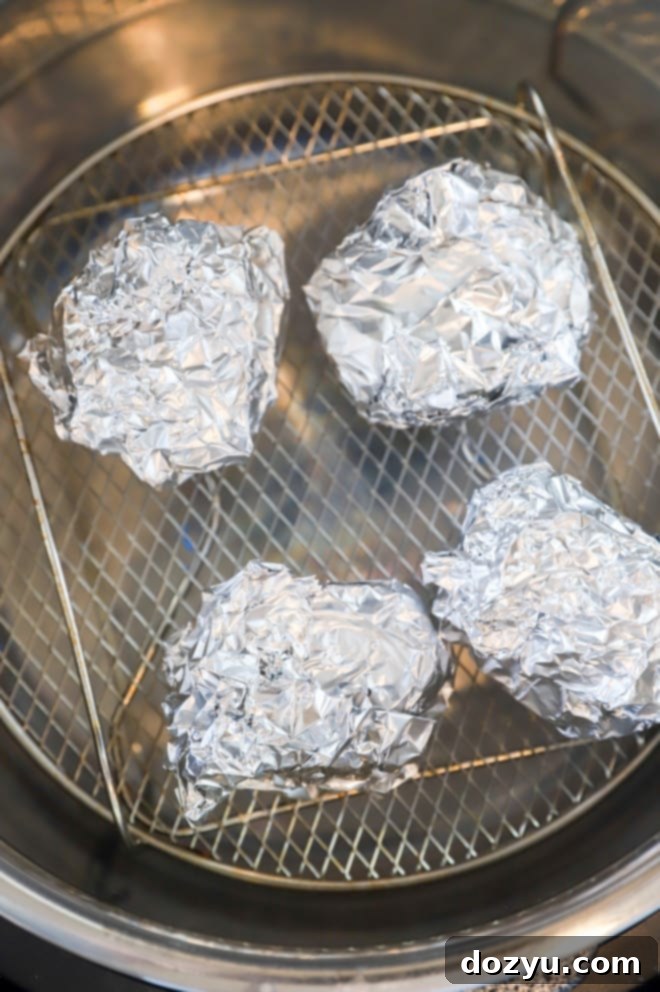 Wrapped garlic bulbs placed inside an air fryer basket, ready for cooking.