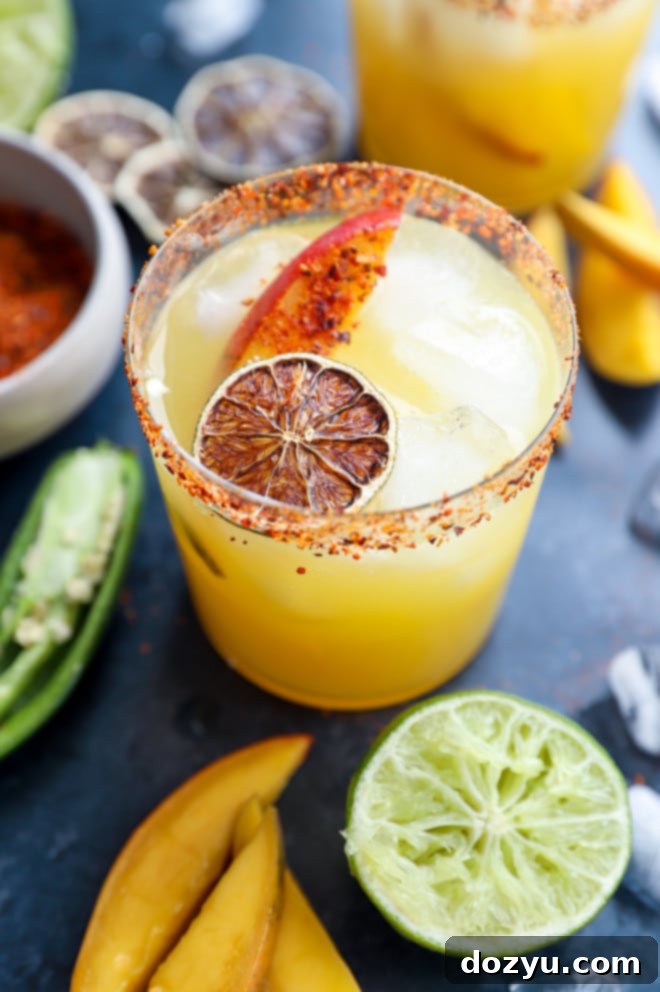 Cocktail in a glass with mango and lime garnish, chili rim